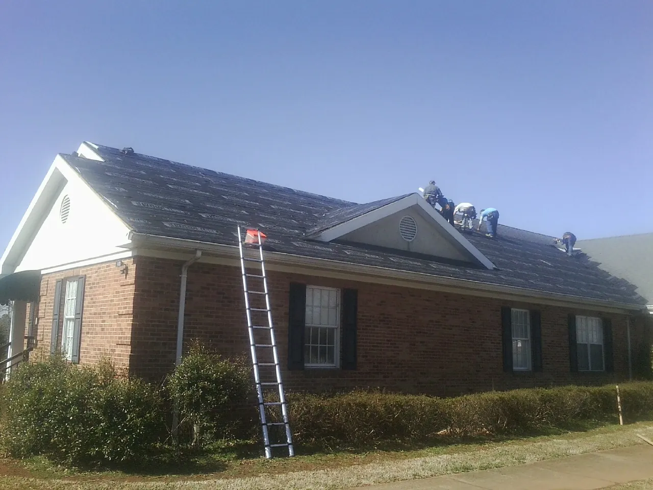 Crew tearing shingles off a brick ranch roof with a ladder set — Metal Roof Repair work by our crew in Lucerne Valley
