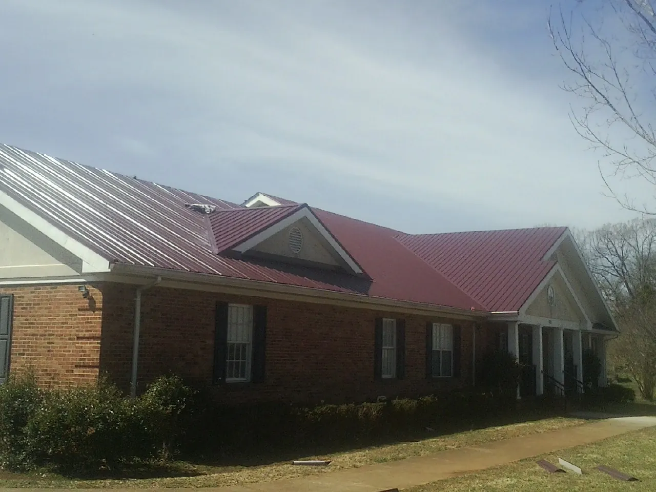 Red metal roof with gabled entries on a long brick building, from a Hail Damage Roof Repair job in Lucerne Valley