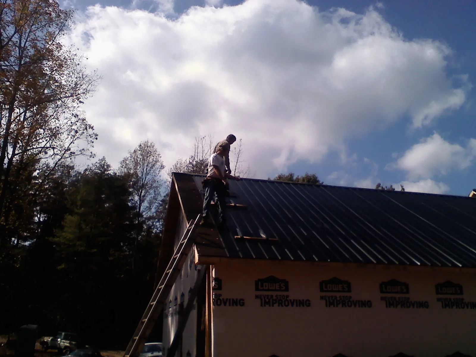 Roofer fastening dark metal panels high against a cloudy sky, from a Roof Inspection job in Lucerne Valley